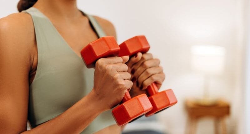 Young African American woman exercising at home in a living room, holding dumbbells